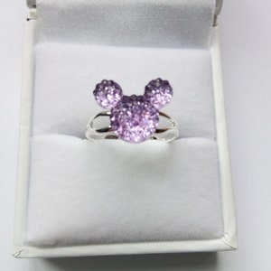 K&ouml;nnte beinhalten: Ein silberner Ring mit einem funkelnden lila Mickey Mouse Kopfdesign.