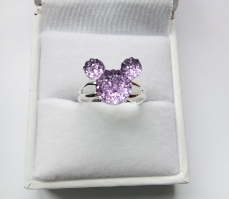 K&ouml;nnte beinhalten: Ein silberner Ring mit einem funkelnden lila Mickey Mouse Kopfdesign.