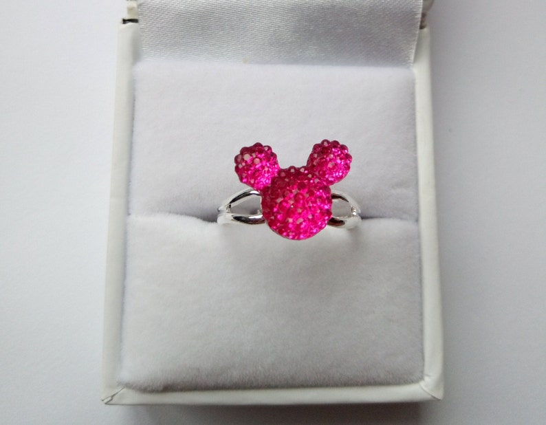 K&ouml;nnte beinhalten: Ein silberner Ring mit einem pinkfarbenen, glitzernden Mickey-Maus-Kopf-Design.