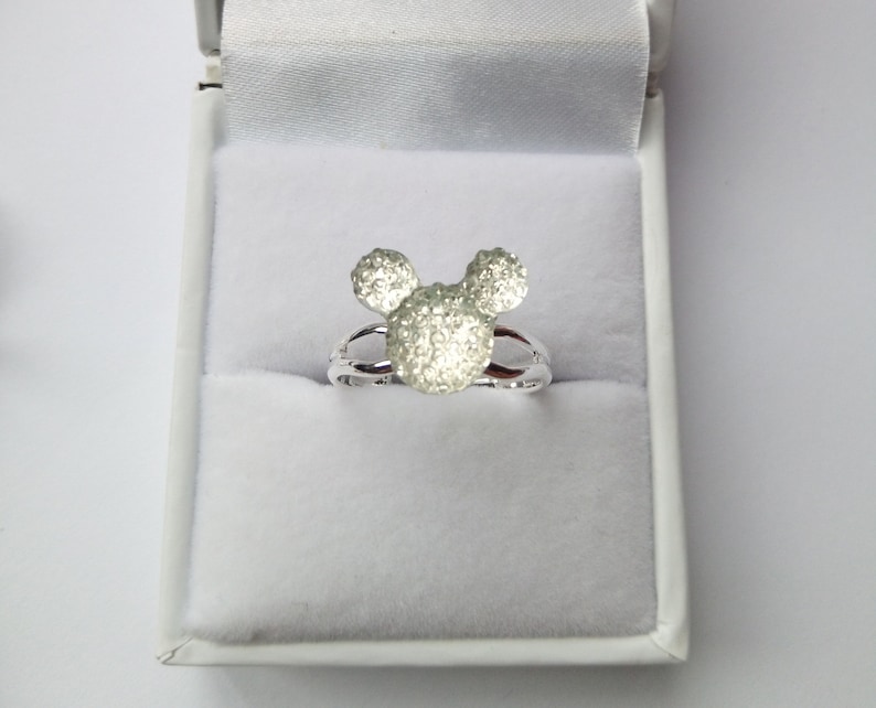 K&ouml;nnte beinhalten: Ein silberner Ring mit einem Mickey-Maus-Kopf-Design. Der Kopf besteht aus kleinen, funkelnden Steinen.