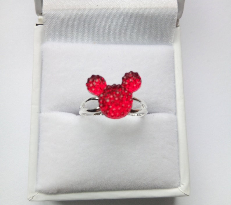 May include: A silver ring with a red Mickey Mouse head design. The head is made of small red rhinestones.