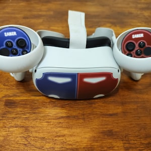 May include: A white virtual reality headset with two white controllers. The controllers have blue and red faceplates with the word "SABER" printed on them.