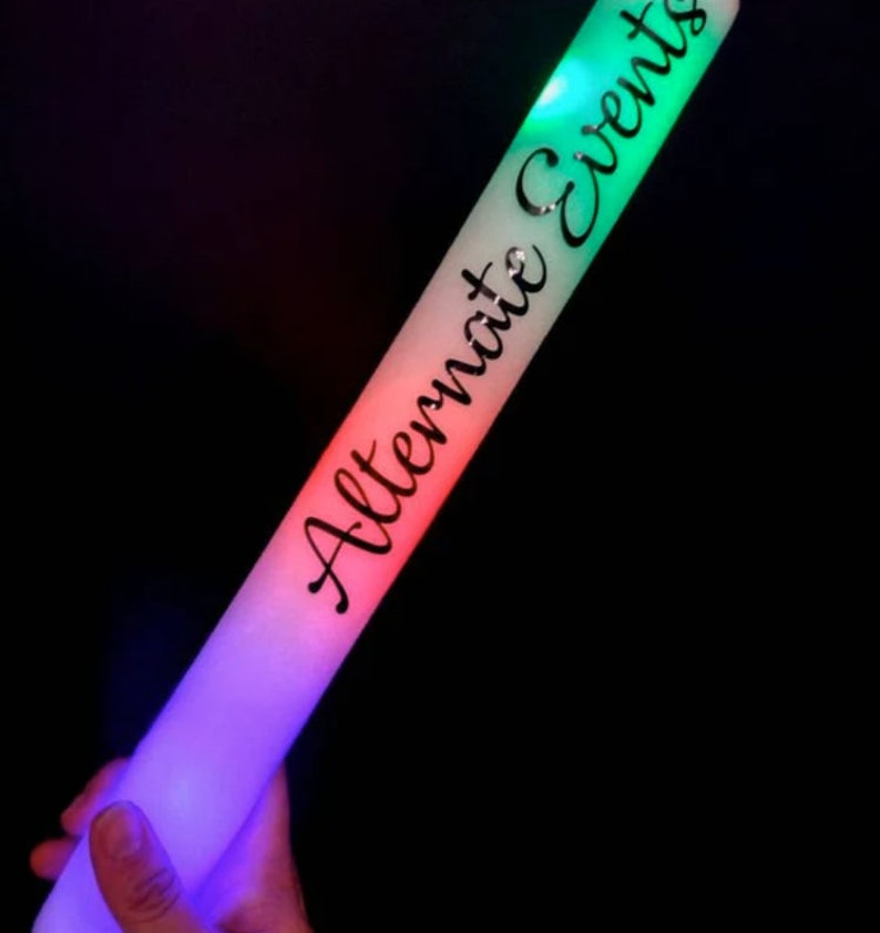May include: A glowing foam stick with the text "Alternate Events" in black script. The stick transitions from purple to red to green, with the text running along the length of the stick. The background is black.