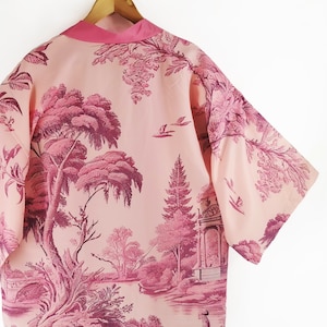 Puede incluir: Un kimono de manga corta con estampado floral rosa y burdeos. El kimono tiene un estilo japonés tradicional con un cuello ancho y un cierre de nudo.