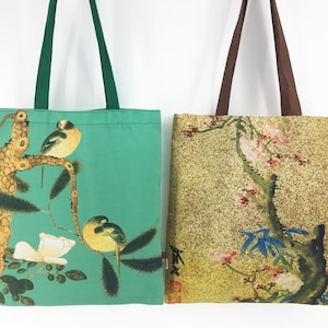 Puede incluir: Dos bolsas de mano de tela. Una tiene un fondo verde azulado con un diseño de pájaros y flores, y asas verdes. La otra tiene un fondo dorado con un estampado floral y de ramas de árboles, y asas marrones. Ambas bolsas son rectangulares.