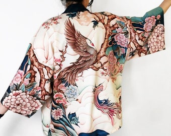 May include: A white kimono with a floral print featuring a phoenix and a tree with pink flowers. The kimono has a blue and green background.