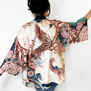 May include: A white kimono with a floral print featuring a phoenix and a tree with pink flowers. The kimono has a blue and green background.