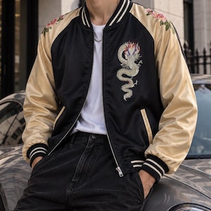 May include: A black and gold satin bomber jacket featuring a white dragon embroidery on the chest, floral patterns on the shoulders, and striped ribbed trim on the collar and cuffs, worn over a plain white t-shirt and dark cargo pants.