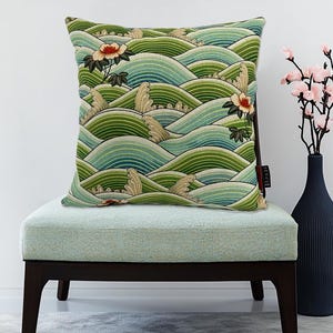 May include: A green and blue patterned throw pillow with a wave design and floral accents. The pillow is sitting on a light blue chair with dark brown legs.