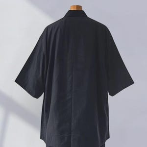 May include: A black short-sleeved shirt with a collar. The shirt is made of a textured fabric and has a relaxed fit.