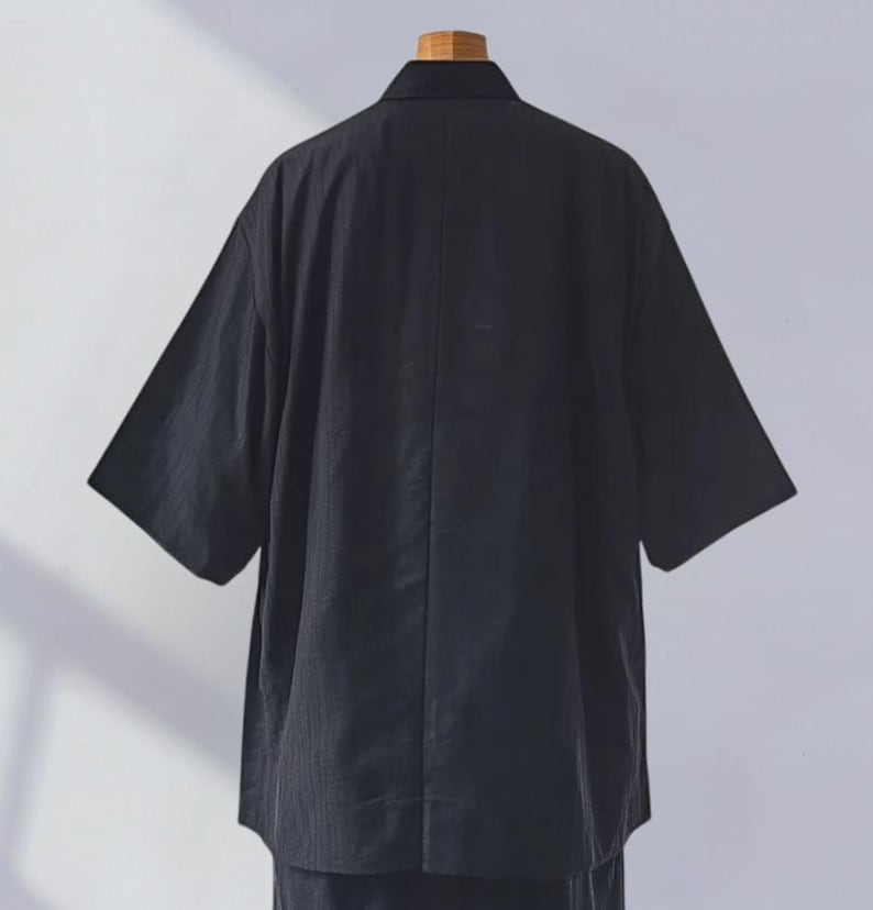 May include: A black short-sleeved shirt with a collar. The shirt is made of a textured fabric and has a relaxed fit.