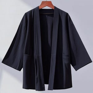 May include: A dark blue lightweight kimono-style jacket with long sleeves and a wide open front. The jacket has two pockets on the sides and is made of a soft, comfortable fabric.