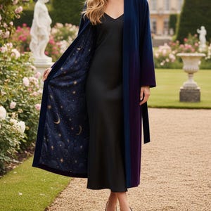 May include: A long, open-front robe in navy blue and purple. The robe's interior features a celestial pattern of gold stars and crescent moons on a dark blue background. The robe is worn over a black dress and paired with black heels.