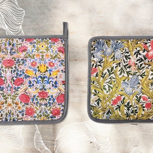 May include: Two square pot holders with floral patterns. One pot holder has a red, yellow, and blue floral pattern. The other pot holder has a green, yellow, and blue floral pattern. Both pot holders have a gray border.