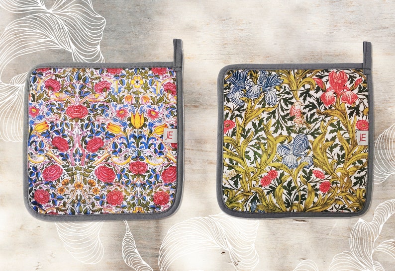 May include: Two square pot holders with floral patterns. One pot holder has a red, yellow, and blue floral pattern. The other pot holder has a green, yellow, and blue floral pattern. Both pot holders have a gray border.