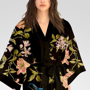May include: A black velvet robe with a floral print featuring pink, white, and green flowers. The robe has a V-neck and a sash tie.
