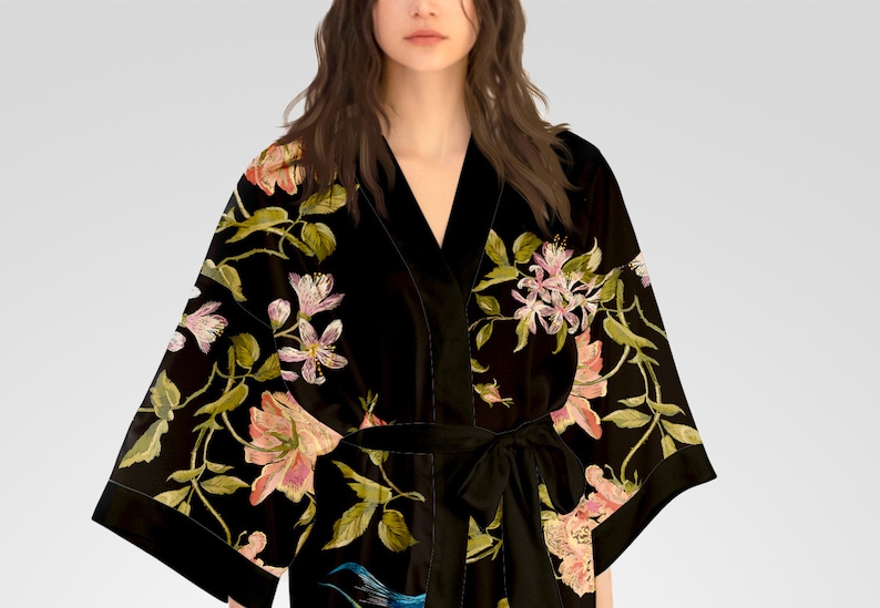 May include: A black velvet robe with a floral print featuring pink, white, and green flowers. The robe has a V-neck and a sash tie.