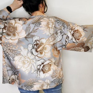 Puede incluir: Un kimono de seda gris con estampado floral que presenta un pájaro y hojas en tonos marrones y dorados.