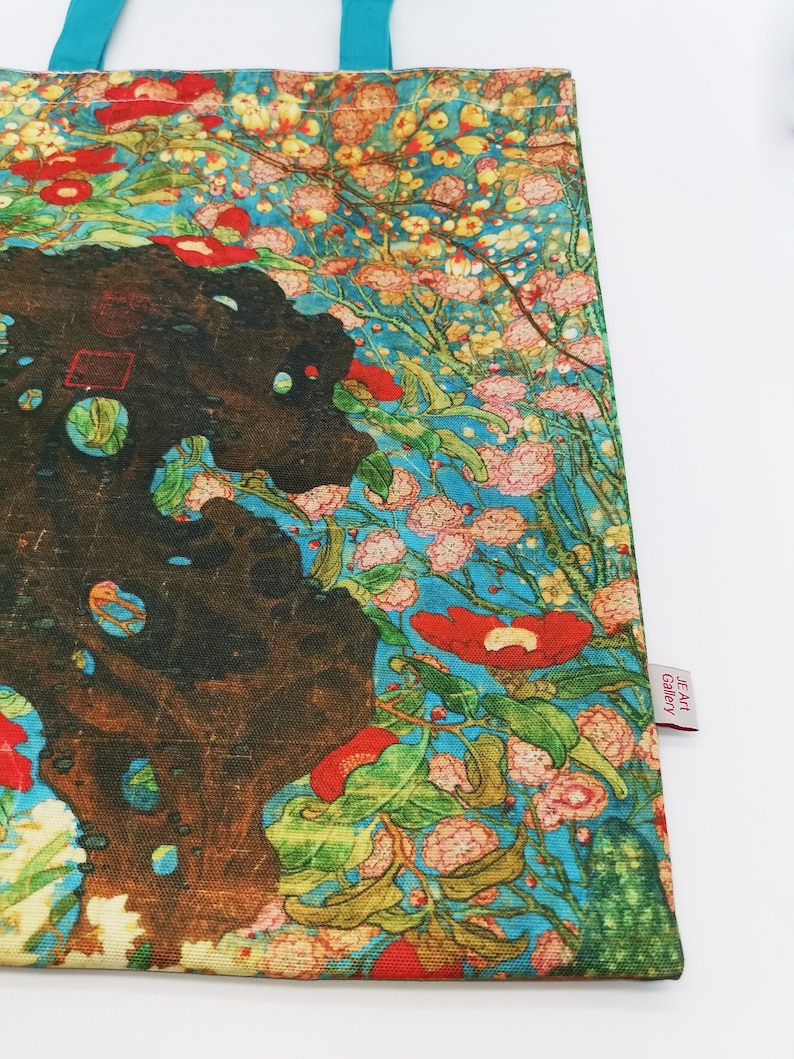 May include: A tote bag with a colorful floral print featuring red, pink, and white flowers on a blue background. The bag has a turquoise handle and a small tag that says "JE Art Gallery".