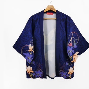 Puede incluir: Un kimono azul marino con estampado floral con flores azules, naranjas y blancas. El kimono tiene un cuello ancho y mangas tres cuartos.
