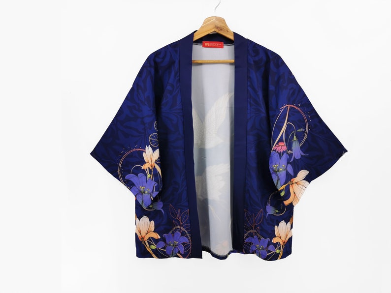 Puede incluir: Un kimono azul marino con estampado floral con flores azules, naranjas y blancas. El kimono tiene un cuello ancho y mangas tres cuartos.