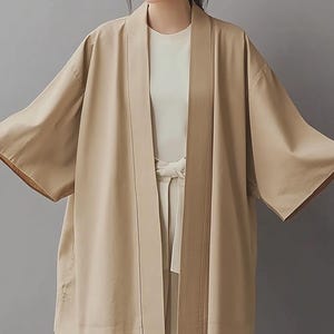 May include: A long, light brown kimono-style cardigan with a shawl collar and a sash tie. The cardigan has a relaxed fit and is made of a lightweight fabric.