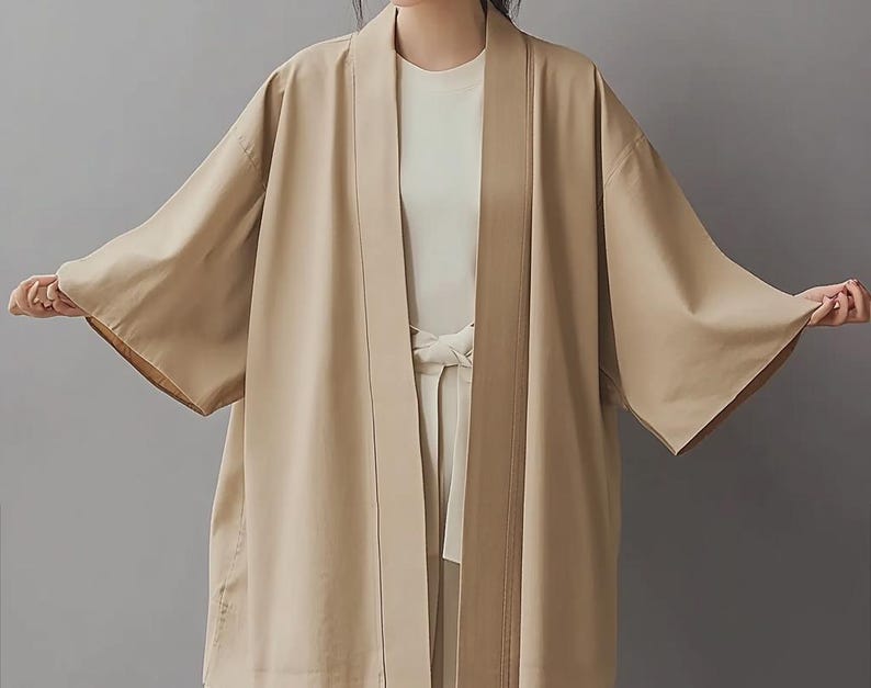 May include: A long, light brown kimono-style cardigan with a shawl collar and a sash tie. The cardigan has a relaxed fit and is made of a lightweight fabric.