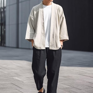 May include: A light beige kimono-style jacket with three-quarter sleeves, worn over a white t-shirt. The jacket is paired with black, loose-fitting trousers. The outfit is casual and suitable for everyday wear.