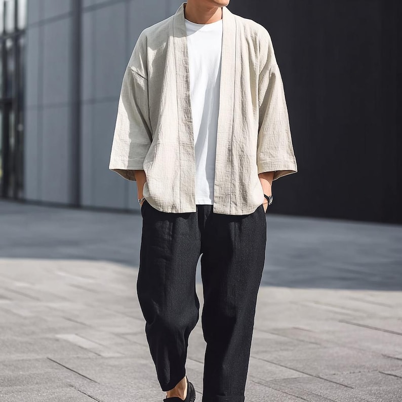May include: A light beige kimono-style jacket with three-quarter sleeves, worn over a white t-shirt. The jacket is paired with black, loose-fitting trousers. The outfit is casual and suitable for everyday wear.