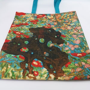 May include: A tote bag with a colorful floral design featuring red, pink, and white flowers on a blue background. The bag has turquoise handles and a small tag with the text "Art Gallery".