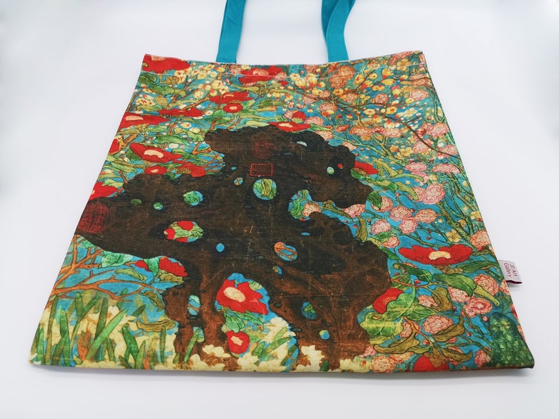 May include: A tote bag with a colorful floral design featuring red, pink, and white flowers on a blue background. The bag has turquoise handles and a small tag with the text "Art Gallery".
