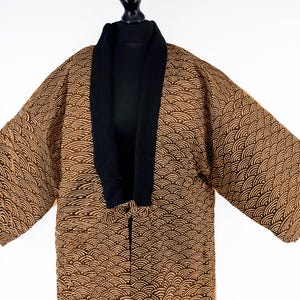 Peut inclure: Kimono marron et noir avec un motif de vagues. Le kimono a un col noir et est présenté sur un mannequin noir. Les manches sont larges et le tissu semble être une matière douce.