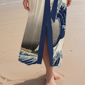 May include: A white maxi dress with a blue and white print of a wave. The dress has a deep V-neckline and a side slit.