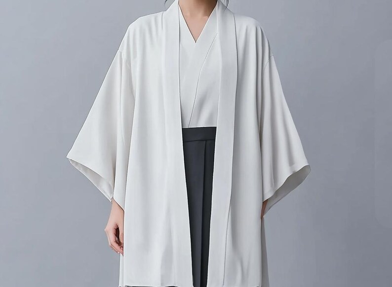 May include: A white kimono with long sleeves and a wide collar. The kimono is open in the front, revealing a white undershirt and black pants.