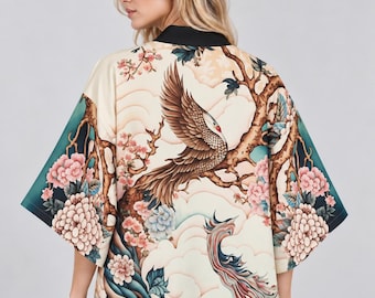 May include: A cream-colored kimono jacket featuring a black collar and wide sleeves. The fabric displays a detailed print of a brown bird perched on a tree branch, surrounded by pink and blue floral clusters, stylized clouds, and a flowing tail design.