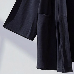 May include: A dark blue lightweight kimono-style jacket with a single pocket on the left side. The jacket has a simple design and is made of a soft, breathable fabric.