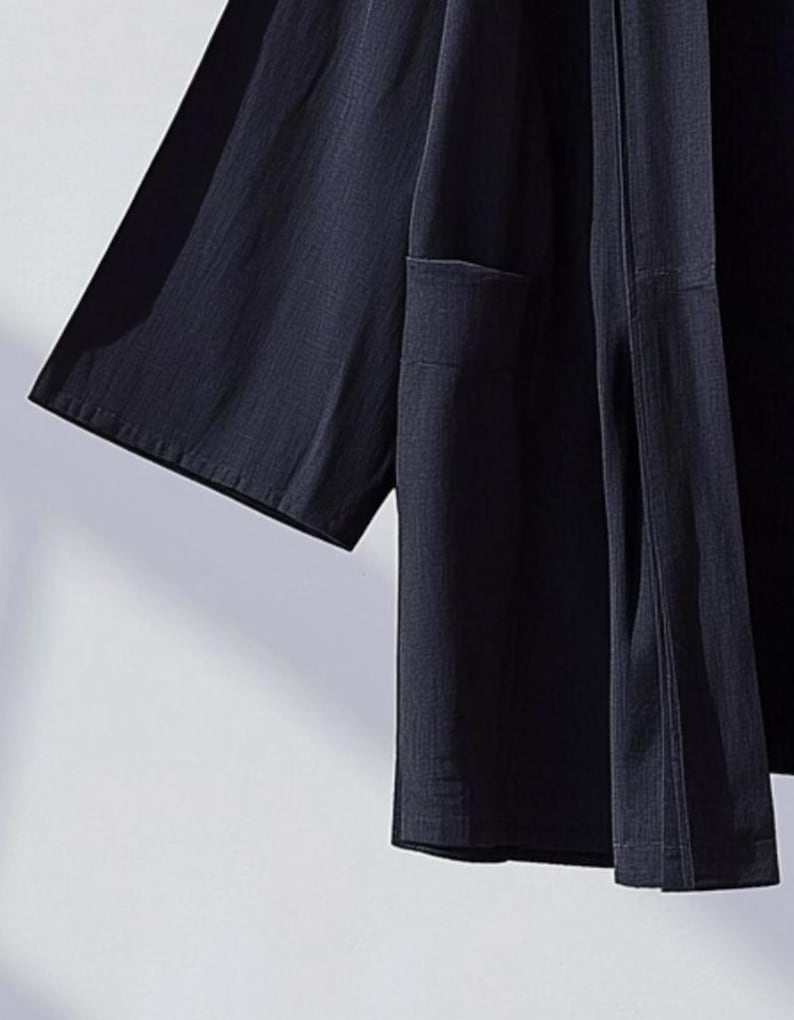May include: A dark blue lightweight kimono-style jacket with a single pocket on the left side. The jacket has a simple design and is made of a soft, breathable fabric.