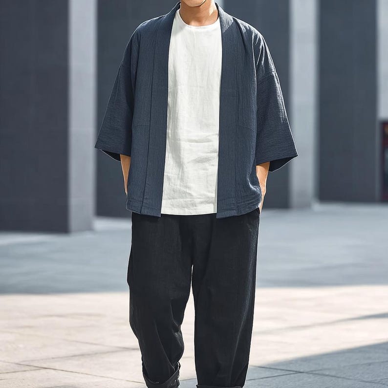 May include: A navy blue kimono-style jacket with wide sleeves, worn over a white t-shirt and paired with black trousers. The jacket has a relaxed fit and a simple, open front design. The outfit is casual and modern.
