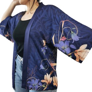 Puede incluir: Un kimono azul marino con estampado floral con flores rosas, moradas y naranjas. El kimono tiene un acabado satinado y un cierre de nudo.