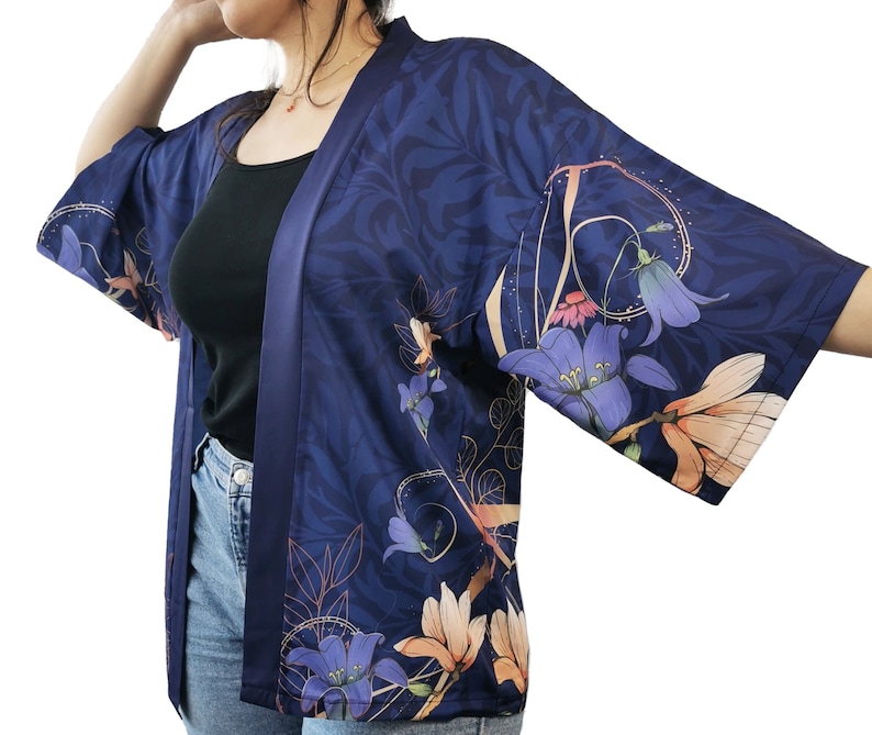 Puede incluir: Un kimono azul marino con estampado floral con flores rosas, moradas y naranjas. El kimono tiene un acabado satinado y un cierre de nudo.
