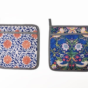 May include: Two gray and white pot holders with floral patterns. One pot holder has a blue and white floral pattern with orange flowers. The other pot holder has a blue background with a floral pattern in shades of pink, yellow, green, and orange. Both pot holders have a gray border.