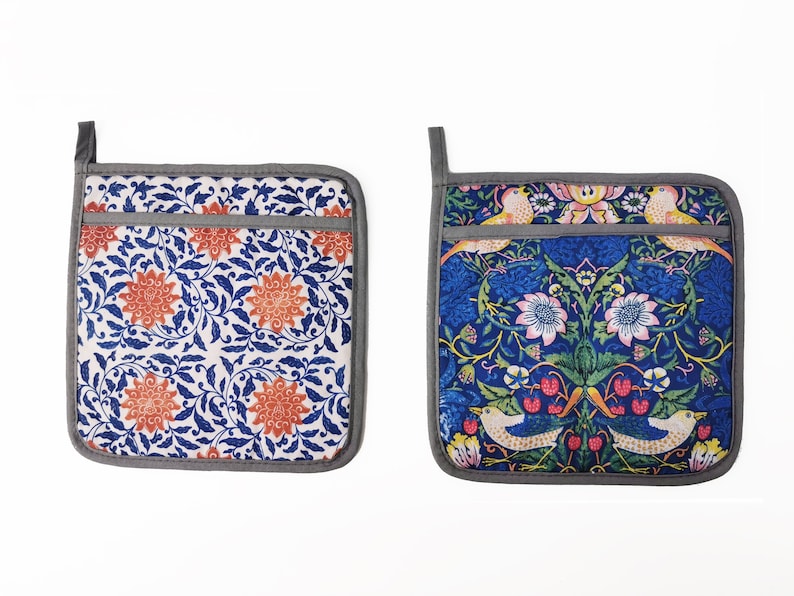 May include: Two gray and white pot holders with floral patterns. One pot holder has a blue and white floral pattern with orange flowers. The other pot holder has a blue background with a floral pattern in shades of pink, yellow, green, and orange. Both pot holders have a gray border.
