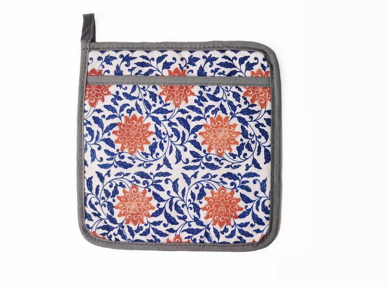May include: A square pot holder with a floral pattern. The pot holder is white with blue and orange floral designs. The pot holder has a gray border.