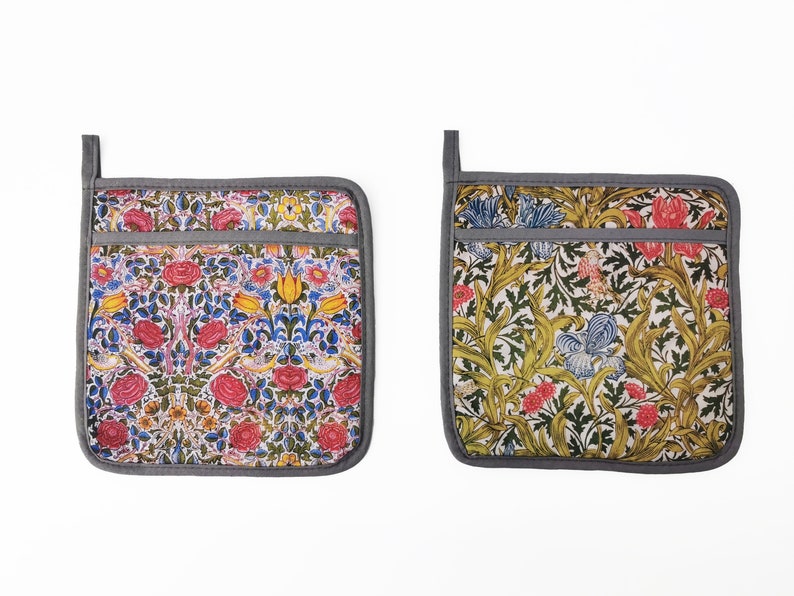 May include: Two gray and white floral patterned pot holders with a gray border. The pot holders have a pocket on the front.
