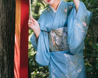 May include: A light blue kimono with floral patterns and a decorative obi belt. The sleeves and lower portion of the kimono feature delicate floral designs in white and pink. The obi belt has a floral pattern with silver and gold accents.