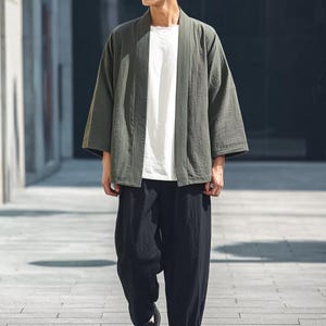 May include: A green kimono-style jacket, white t-shirt, and black trousers. The jacket has a relaxed fit and wide sleeves. The trousers are loose-fitting. The outfit is casual and comfortable, suitable for everyday wear.