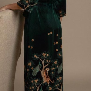 May include: A dark green velvet robe with a detailed tree and animal print. The robe features a wrap-around design with a matching belt. The print includes tigers, peacocks, and flowering trees. The robe has three-quarter sleeves and is knee-length.