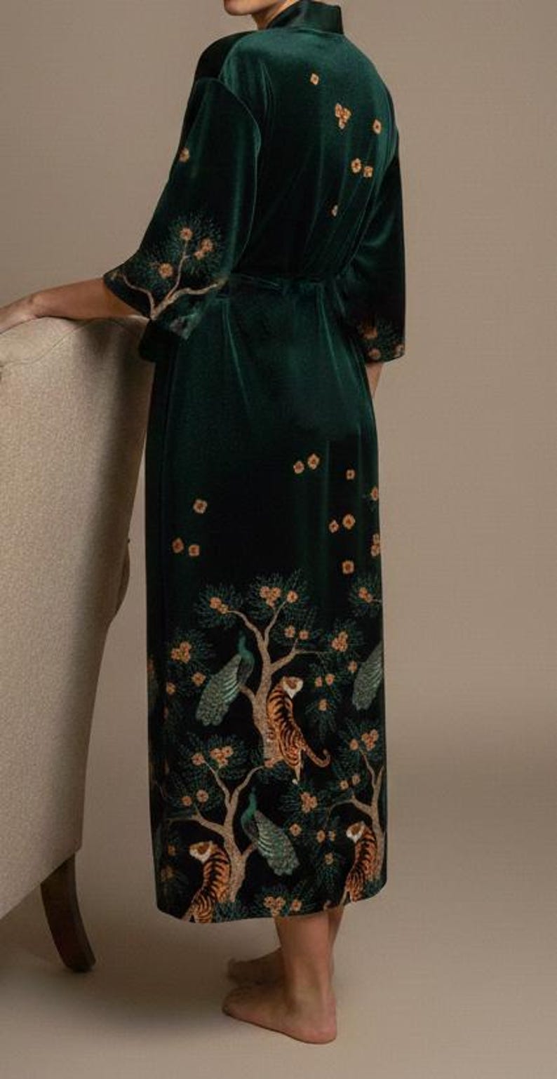 May include: A dark green velvet robe with a detailed tree and animal print. The robe features a wrap-around design with a matching belt. The print includes tigers, peacocks, and flowering trees. The robe has three-quarter sleeves and is knee-length.