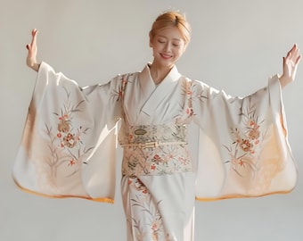 Op de afbeelding: Een crèmekleurige kimono met bloemen- en takpatronen in tinten oranje en bruin. De kimono heeft wijde mouwen en wordt in de taille samengehouden met een patroon obi-riem. De randen van de mouwen zijn afgewerkt met een gouden rand.