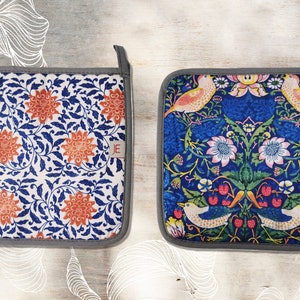 May include: Two square pot holders with a gray border. One pot holder has a white background with a blue and orange floral pattern. The other pot holder has a blue background with a floral pattern featuring birds and berries. Both pot holders have a small white tag with the letter "E" in red.